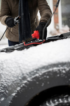 Woman Using Jumper Cables On Car Battery On Snowy Day