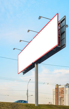 Blank White Billboard On The Highway With Passing Cars On The Background Of Multi-storey City Buildings At Sunset, Mock Up