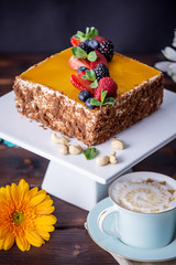 Homemade square cake decorated with yellow jelly on top and berries with mint on dark background
