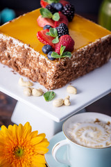 Homemade square cake decorated with yellow jelly on top and berries with mint on dark background