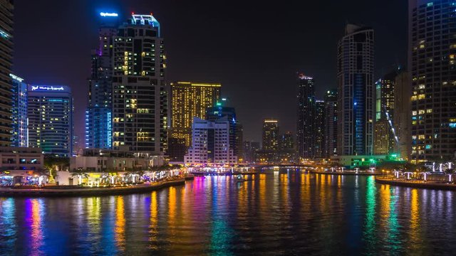 Scenic view of the skyscrapers of Dubai Marina with bright night illumination and a water canal with floating yachts, time lapse, Dubai, UAE