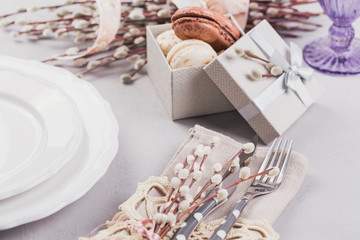 White plate, purple glass, cutlery, present box with macaroons and pussy willow twigs