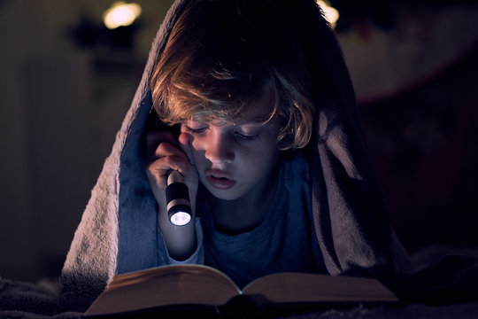 Close up of boy reading book under blanket