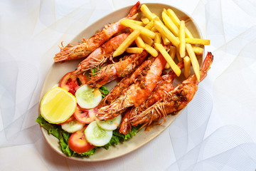 Plate grilled spicy prawn shrimps kebabs, vegetables, french fries with sauces and greens on light background.