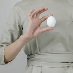 Unrecognizable woman in gray dress holding white egg preparing for Easter holiday. A square size for social networks.