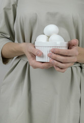 Unrecognizable woman in grey dress holding white eggs preparing for Easter holiday.