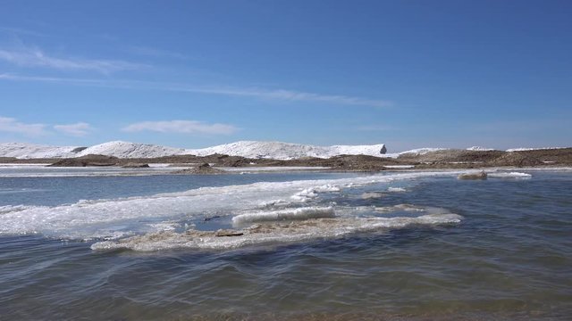 Edge of water with ice and snow along lake shore in winter with blue sky in the background