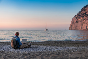 Fototapeta premium young man with laptop working on the beach. Freedom, remote work, freelancer, technology, internet, travel and vacation concepts