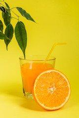 Orange juice in a glass beaker and citrus slices on a yellow background with copy space
