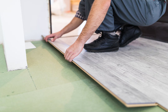 Close up man hands Carpenter worker installing laminate flooring in the new room