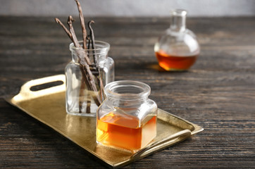 Jars with vanilla extract and sticks on metal tray