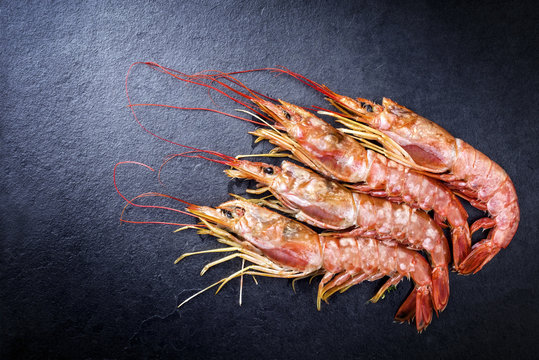 Four raw black tiger prawn as top view on a black board