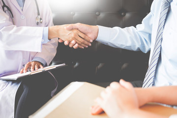Fototapeta premium Doctor shakes hands at medical office with patient, wearing glasses, stethoscope and lab coat.