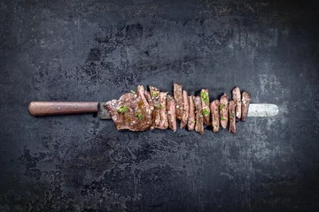Gardinen Traditional barbecue skirt steak sliced as close-up on a knife with copy space © HLPhoto