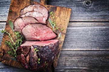 Poster Barbecue dry aged haunch of venison with herbs as close-up on an old cutting board © HLPhoto