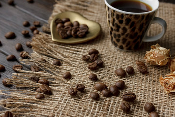 Bronze glass vase with pressed flower on a tablecloth. Golden hearth-shaped saucer with roasted coffee beans. Pure arabica on a wooden table. Lighted candle on the background. Aromatic breakfast