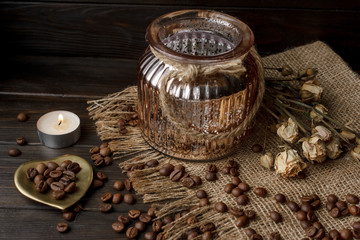 Vase with pressed flower on a tablecloth. Golden hearth-shaped saucer with roasted coffee beans. Pure arabica on a wooden table. Lighted candle on the background. Aromatic breakfast