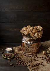 Vase with pressed flower on a tablecloth. Golden hearth-shaped saucer with roasted coffee beans. Pure arabica on a wooden table. Lighted candle on the background. Aromatic breakfast