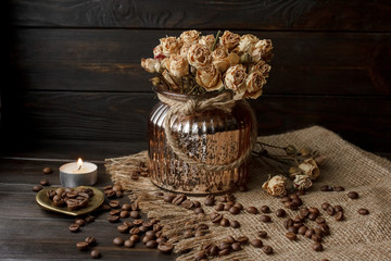 Vase with pressed flower on a tablecloth. Golden hearth-shaped saucer with roasted coffee beans. Pure arabica on a wooden table. Lighted candle on the background. Aromatic breakfast