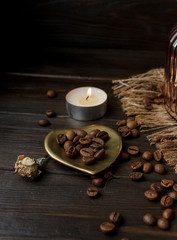 Vase with pressed flower on a tablecloth. Golden hearth-shaped saucer with roasted coffee beans. Pure arabica on a wooden table. Lighted candle on the background. Aromatic breakfast