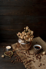 Vase with pressed flower on a tablecloth. Golden hearth-shaped saucer with roasted coffee beans. Pure arabica on a wooden table. Lighted candle on the background. Aromatic breakfast