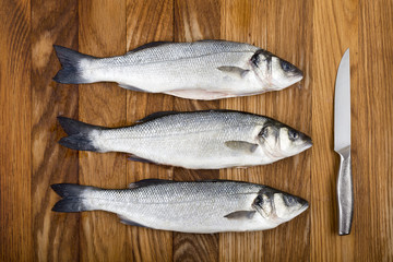 Three European basses with removed scales and steel knife on the wooden oak board