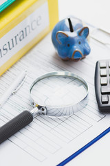 Clean insurance form, piggy bank, magnifying glass, pen and calculator