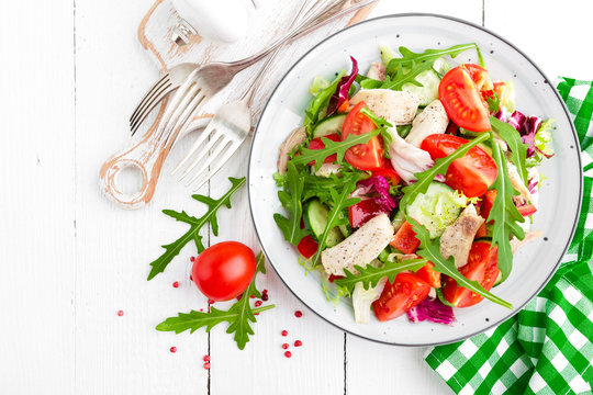 Chicken fillet salad with tomato, lettuce, cucumber and arugula leaves. Fresh vegetable salad with chicken meat. Healthy food. White wooden background. Top view