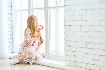 cute little girl looking out the window with flowers hands