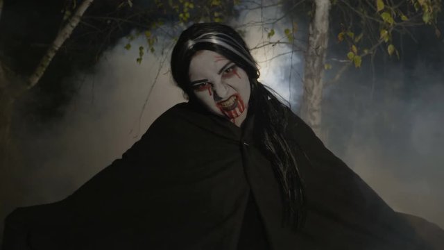 Malefic female zombie vampire getting out from a foggy forest at night in the moonlight to celebrate halloween