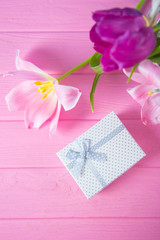 White gift box and tender bouquet of beautiful pink tulips on pink wooden background