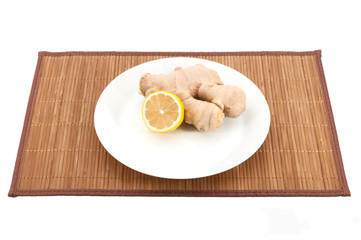 Ginger and lemon on a white plate on a bamboo mat on a white background.