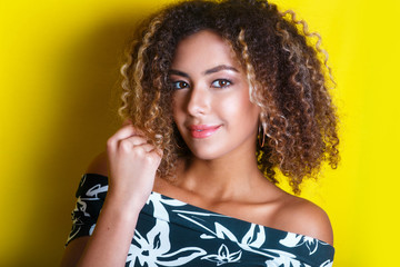 Beauty portrait of young african american girl with afro hairstyle. Girl posing on yellow background, looking at camera.
