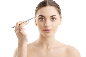 Fototapeta premium Studio shot of a beautiful young woman applying makeup to her eyebrow while standing at isolated background.
