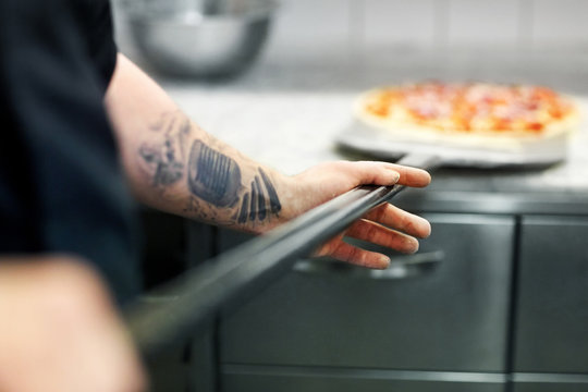 cook or baker hand with pizza on peel at pizzeria