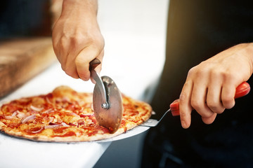 cook hands cutting pizza to pieces at pizzeria
