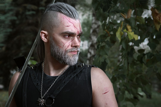 Cosplay, Dressed Like A Hero Geralt Of Rivia From The Game The Witcher, A Fantastic Warrior With A Sword In His Hands