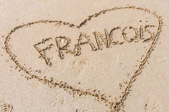 Heart shape with male name inside hand written on wet sand on sunny day. Concept of love and romance