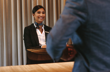 Smiling hotel receptionist attending guest at check-in counter - obrazy, fototapety, plakaty
