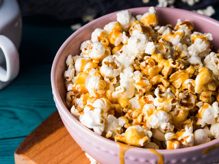Popcorn with salted caramel in pink bowl on wooden board on dark background