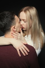 Portrait of a beautiful young couple in love posing at studio over dark background. Guy and girl kissing close up