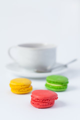 Obraz na płótnie Canvas Traditional french multicolored cakes macarons in the foreground and a cup of tea on a saucer in a blur on a white background