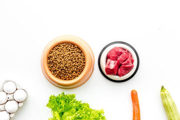 Dry pet food with natural ingredients. Raw meat, vegetables zucchini and carrot near eggs on white backgroud top view copy space
