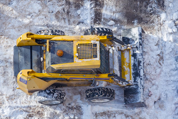 Top view on the yellow snowplow shoveling snow from the road