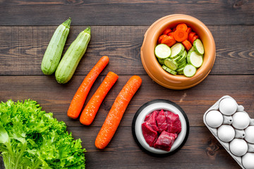 Dry pet food with natural ingredients. Raw meat, vegetables zucchini and carrot near eggs on dark wooden backgroud top view