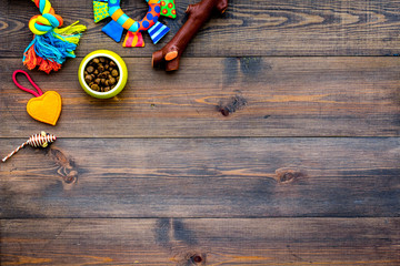 Pet care concept. Toys near bowls with animal feed on dark wooden background top view copy space