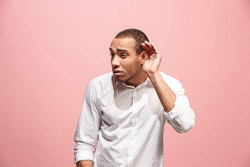 The young man whispering a secret behind her hand over pink background