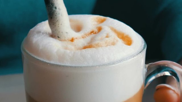 Female hands are stirring the air froth from the latte with straw