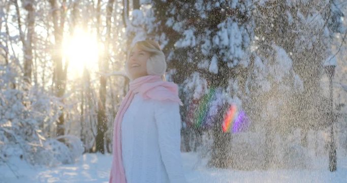 Girl enjoying beautiful winter day outdoors, playing with snow at winter park. Woman wearing a winter white pullover and pink scarf goes down the winter park, sun is shining,