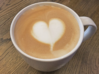 Coffee latte with milk foam designed as heart shape art on wooden table.